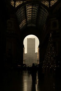 A silhouette views a building through an archway.